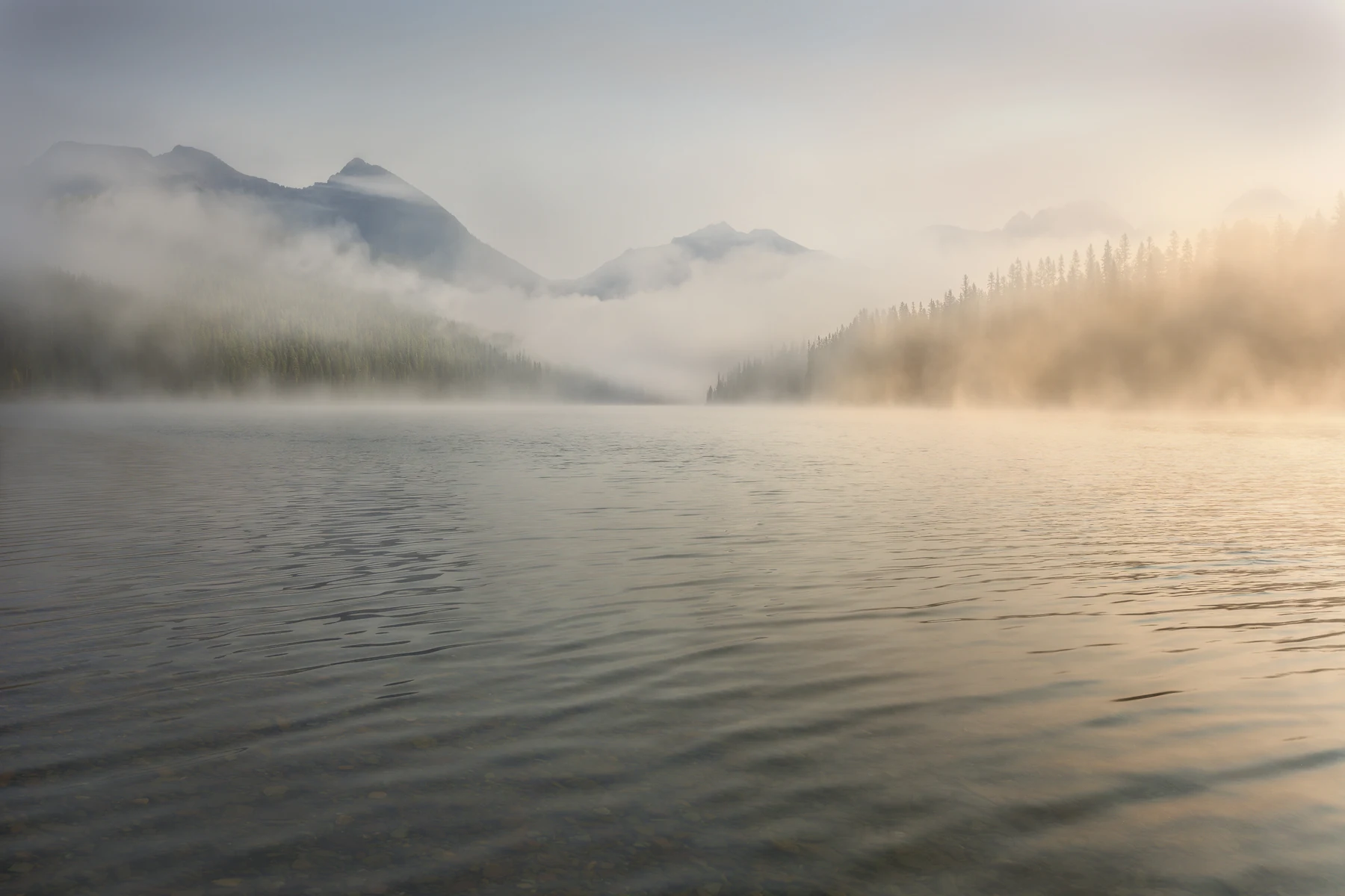 Morning fog lifting from Logging Lake below rugged mountains in Glacier National Park