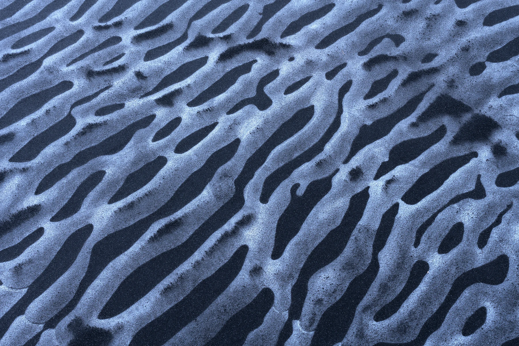 Rippled black sand and pale ice forming an abstract pattern.
