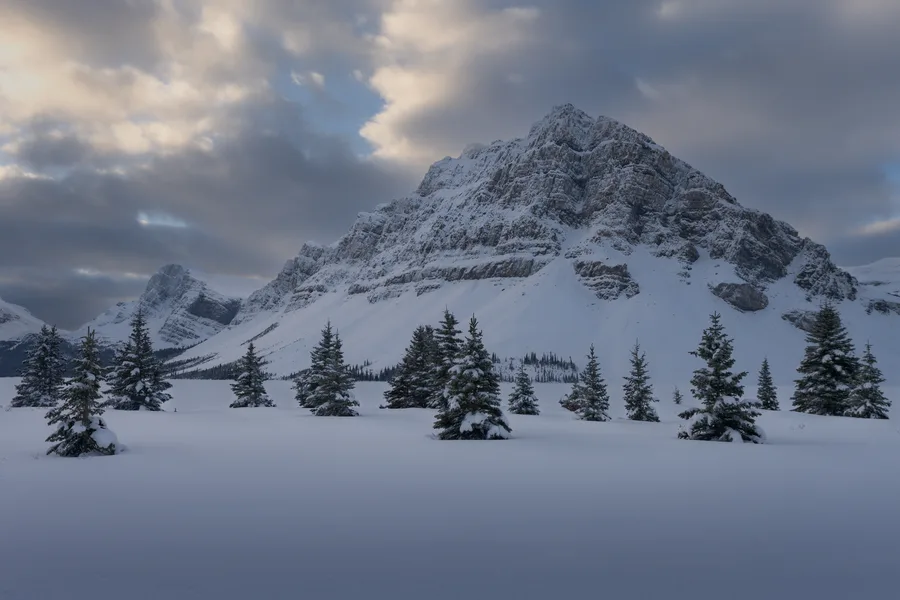 Jagged winter mountain beneath dramatic clouds and snowy trees.