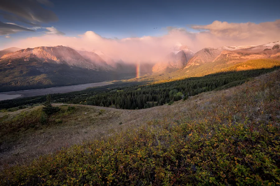 Warm sunrise light touches distant peaks beyond an autumn meadow.