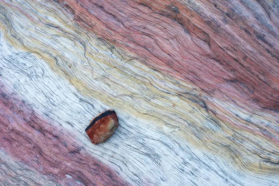 Colorful sandstone stripes with a single small red leaf.
