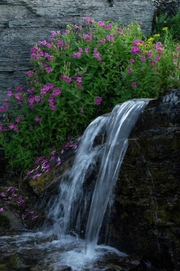 A waterfall flows over rocks in a mountain landscape.