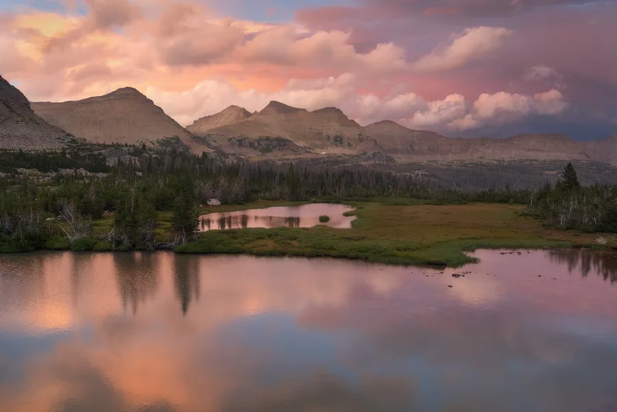 Still mountain lake reflecting pink clouds and distant peaks.