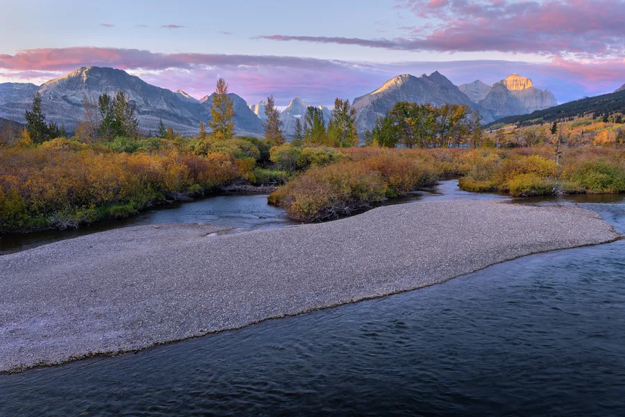A braided river curves toward distant mountains in warm evening light.