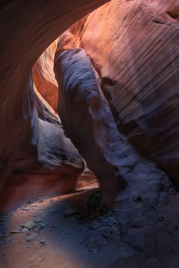 Vertical slot canyon passage with orange sandstone and blue shadow.