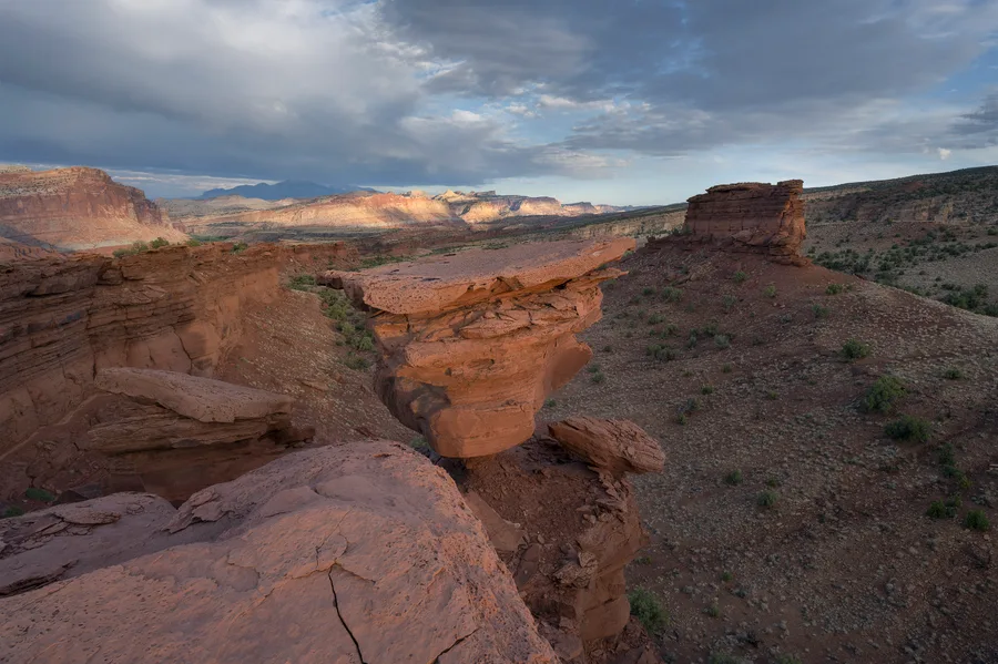 Wide desert canyon with red rock, storm clouds, and warm light.