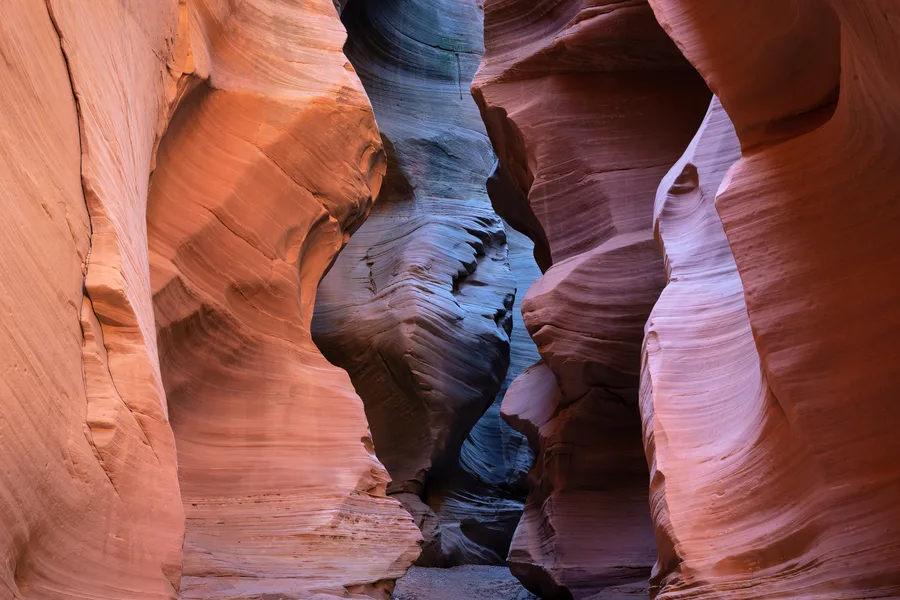Narrow slot canyon with warm orange walls and cool blue shadow.