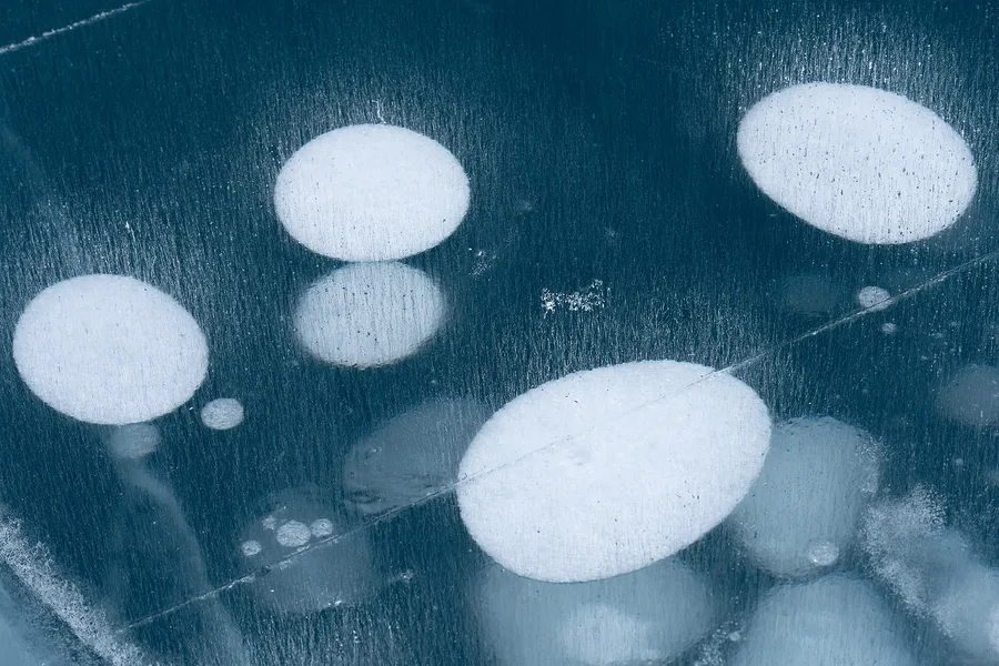 Round white ice bubbles suspended in blue frozen water.