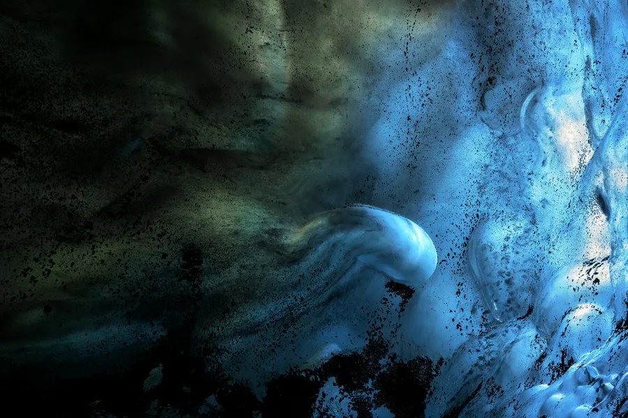 Blue ice cave wall with dark mineral textures and a rounded ice form.