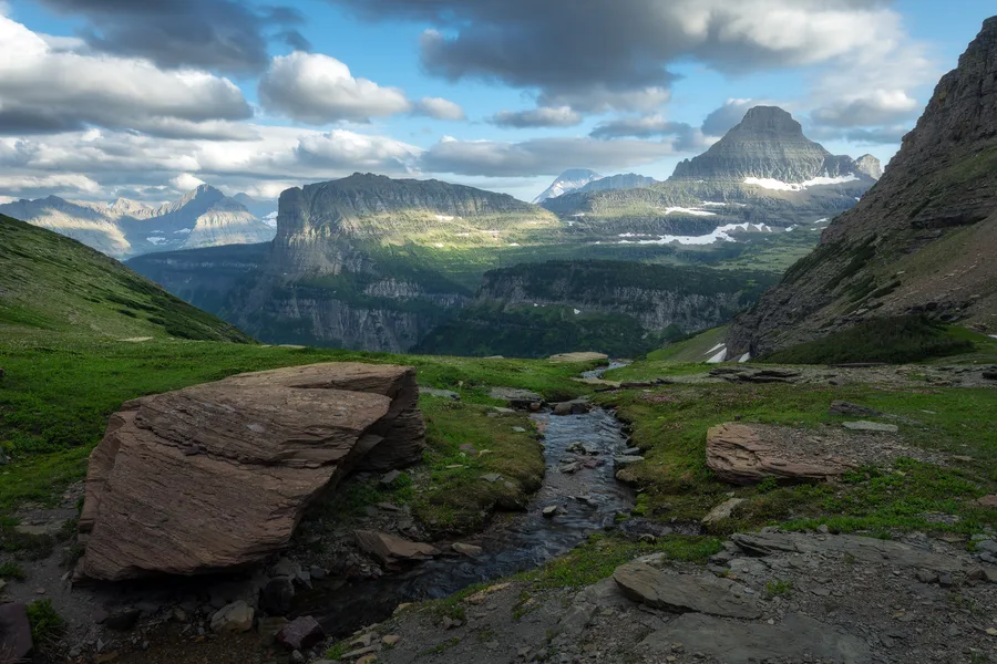 Green mountain valley with river and dramatic clouds.