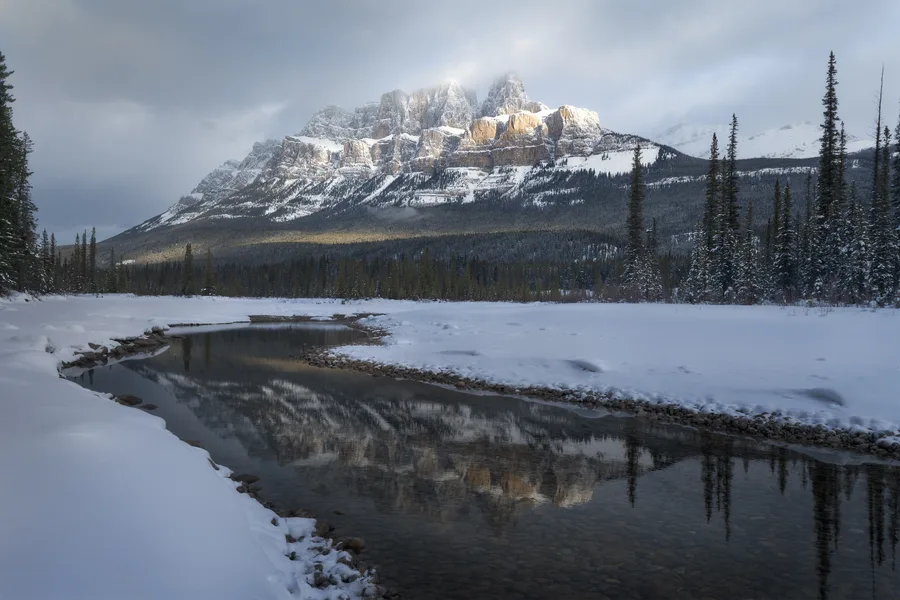 Snowy mountain reflected in a calm winter river bend.
