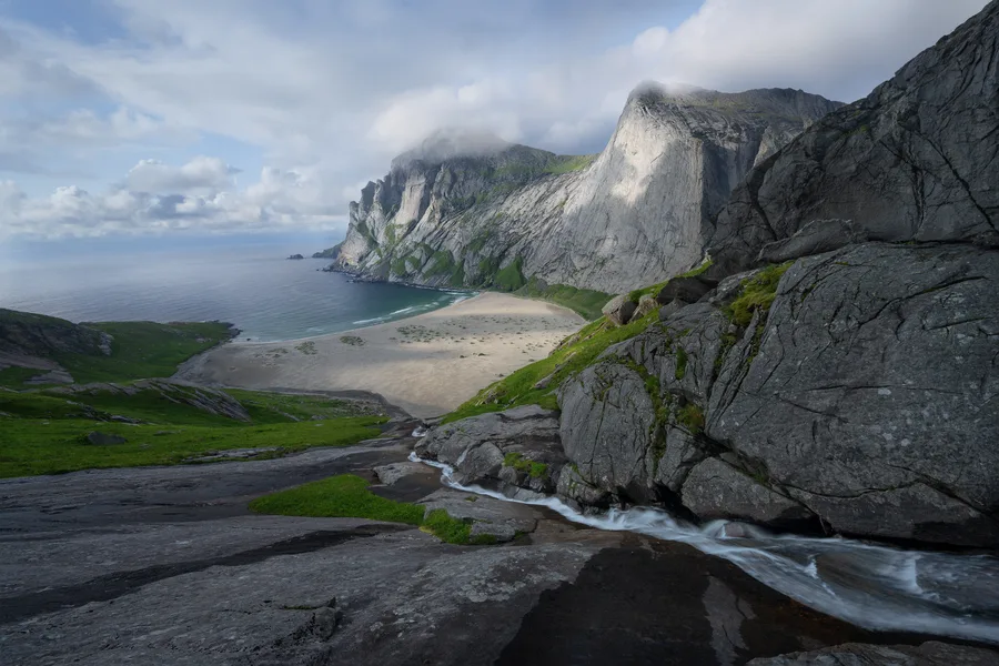 A waterfall flows down to the beach below while towering granite mountains rise thousands of feet.
