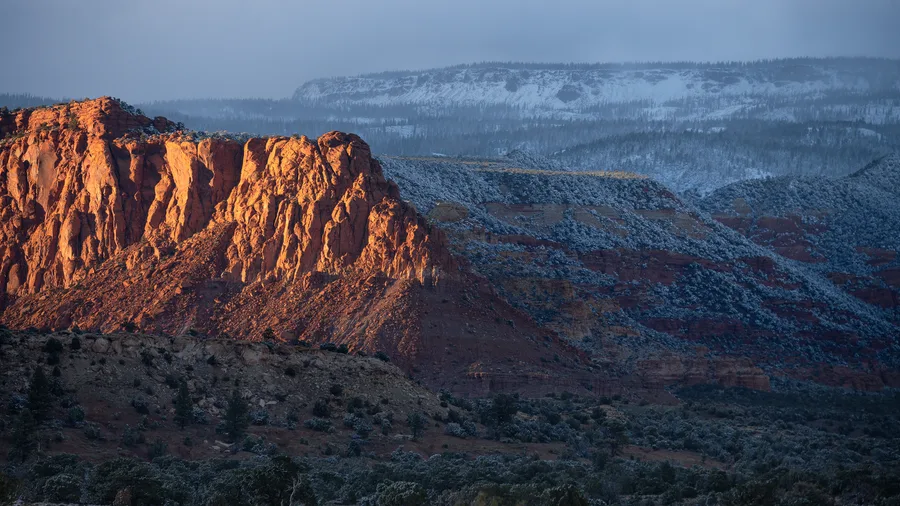 Warm red cliffs rise above a snow-dusted desert plateau.