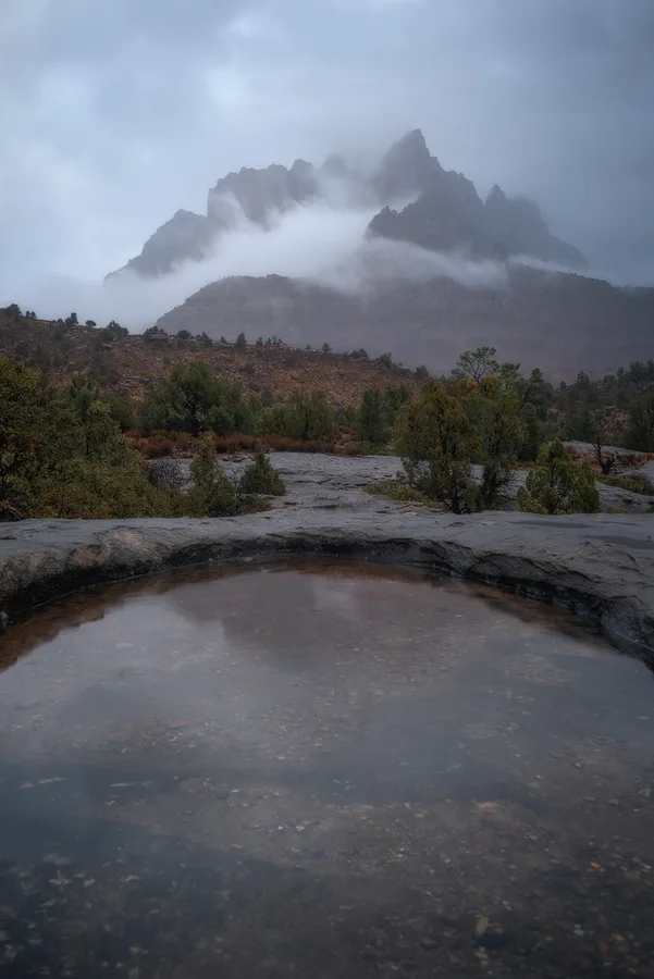 Moody desert pool reflecting a stormy mountain sky.