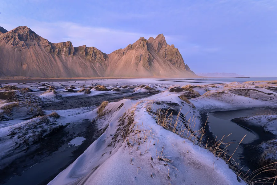 Snowy Iceland mountains and black sand beneath a pastel sky.