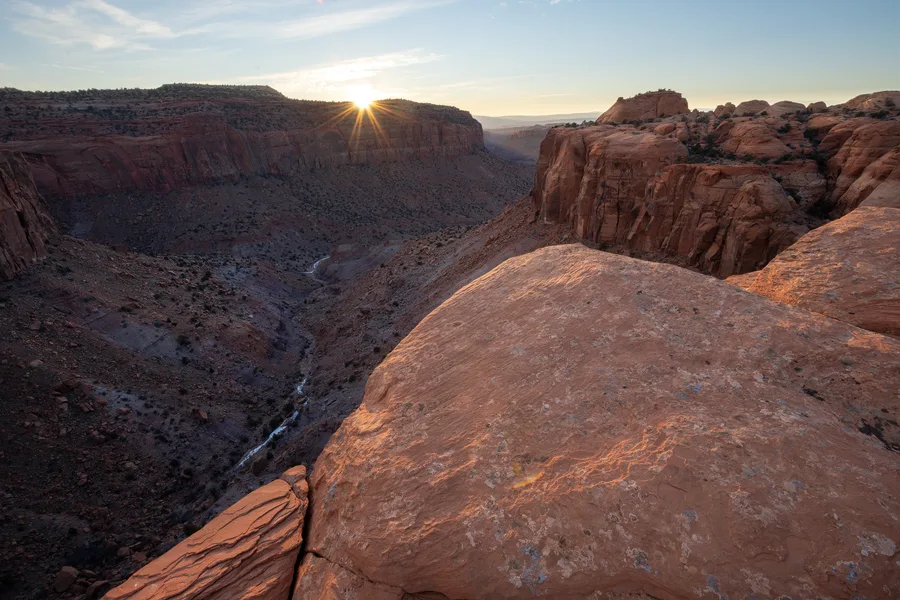 Sunburst over a rounded sandstone canyon rim.