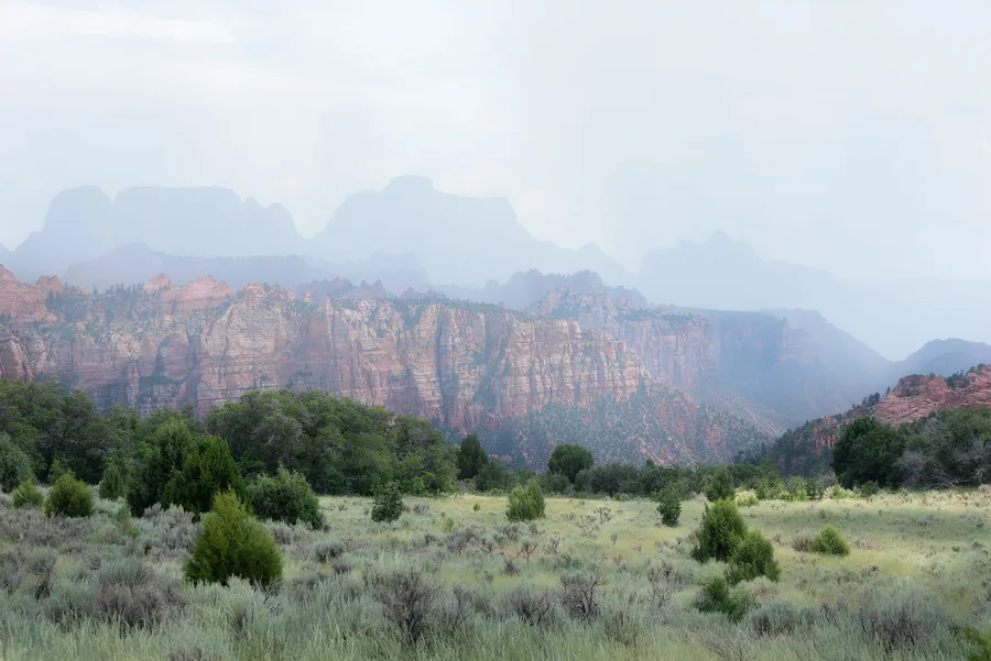 Soft rainy mountain valley with pale cliffs and green foreground.