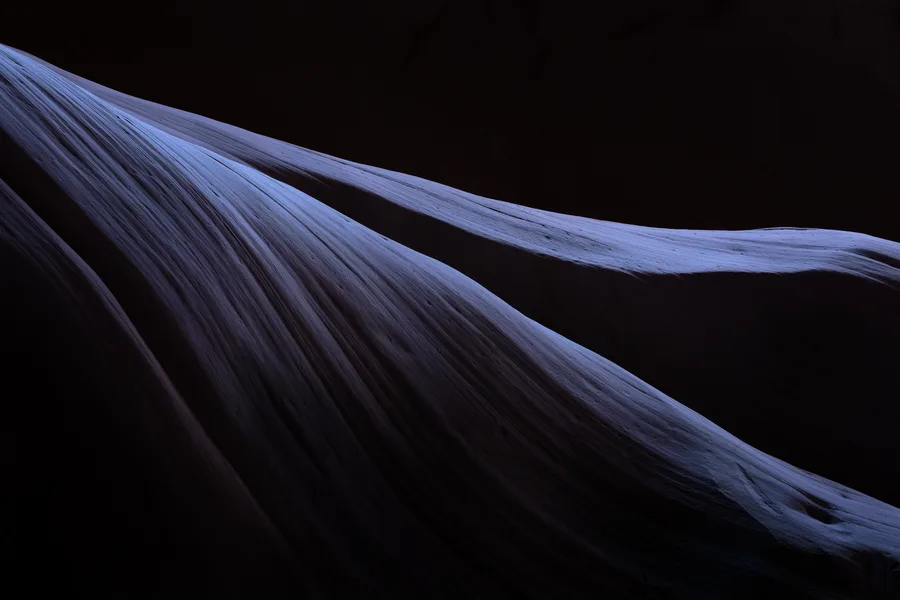 Thin blue light tracing a dark sandstone slot canyon wall.