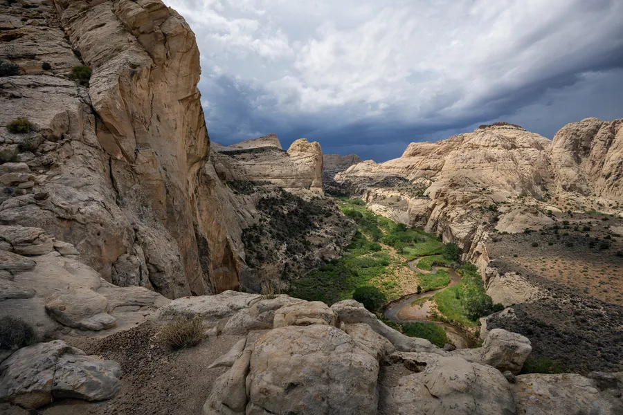 Layered rock cliffs in a canyon beneath a cloudy sky.