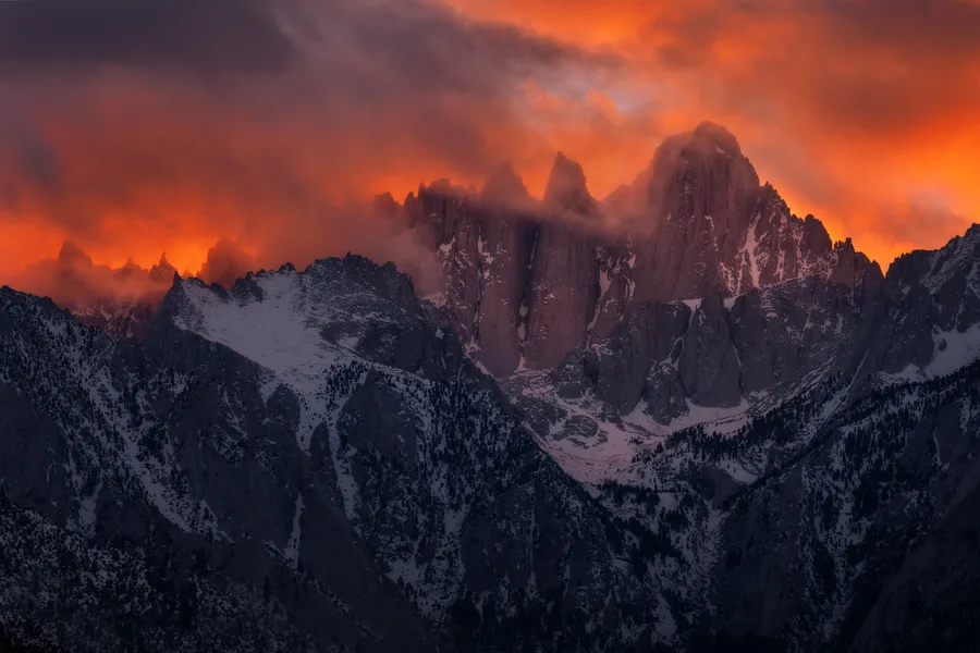 Flaming sunset clouds gather above the dark silhouette of Mount Whitney.