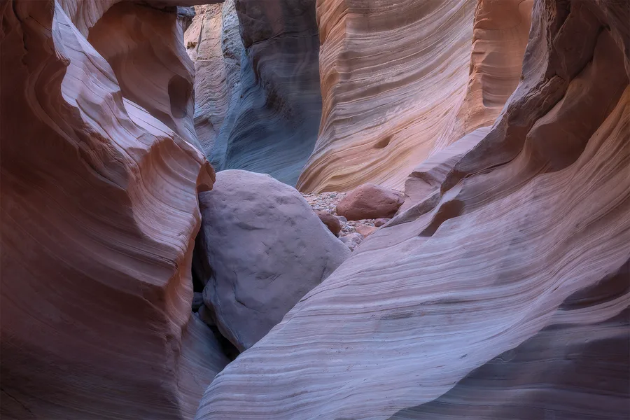 Pale pink and blue sandstone curves inside a slot canyon.