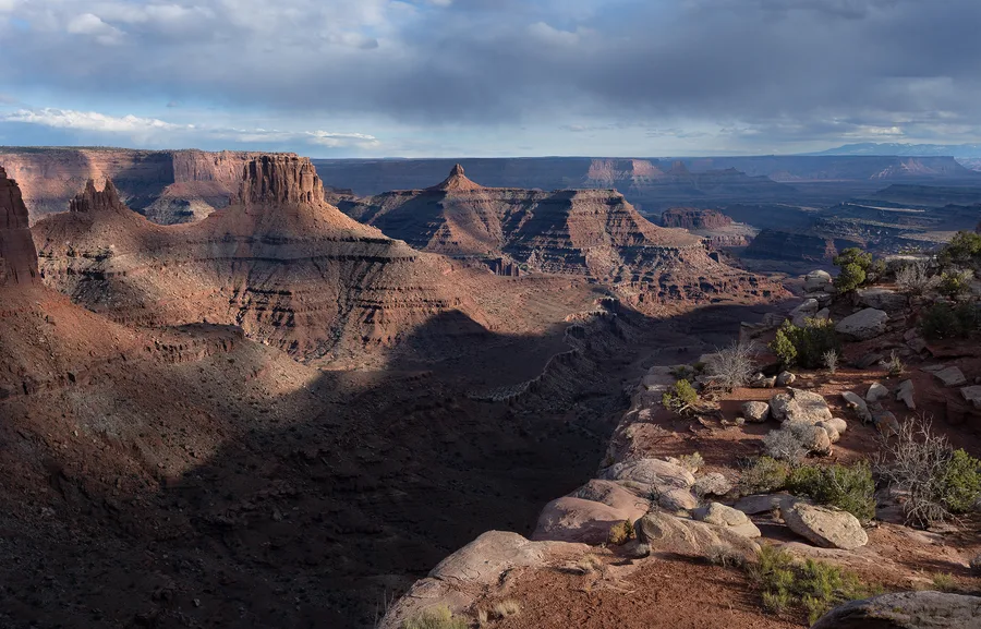 Layered sandstone cliffs in a canyon beneath a cloudy sky.