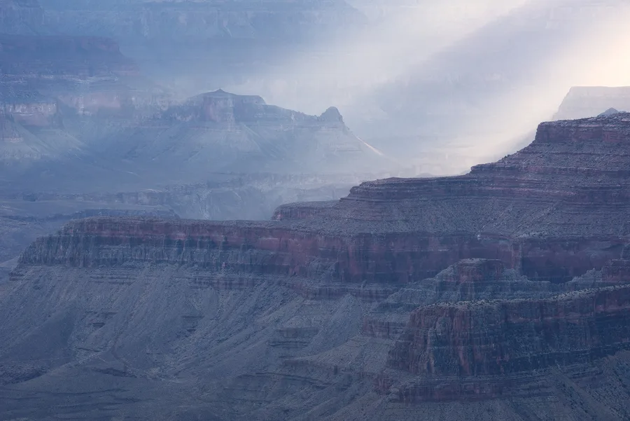 Layered canyon landscape with soft rain and atmospheric light rays.