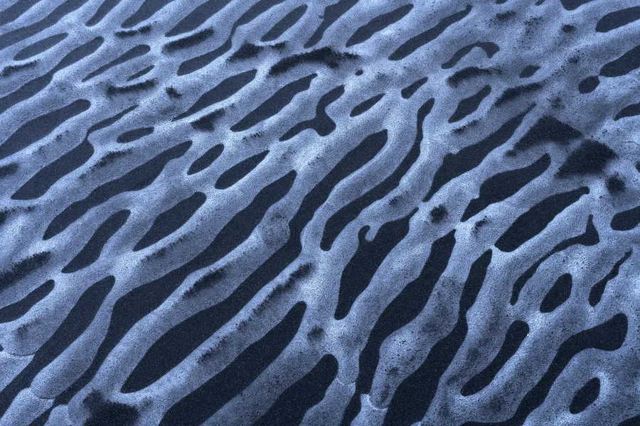 Rippled black sand and pale ice forming an abstract pattern.