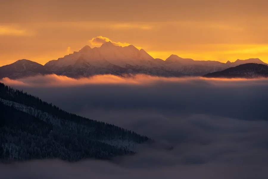 Misty mountains rise beneath a cloudy sky.
