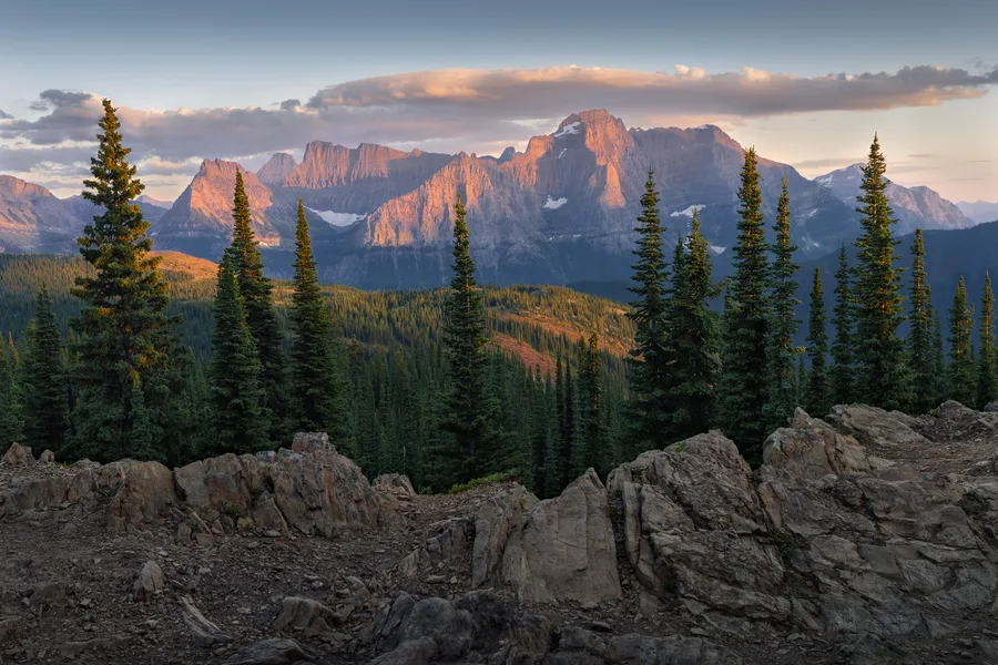 Mountain sunset with forest, river valley, and pink clouds.