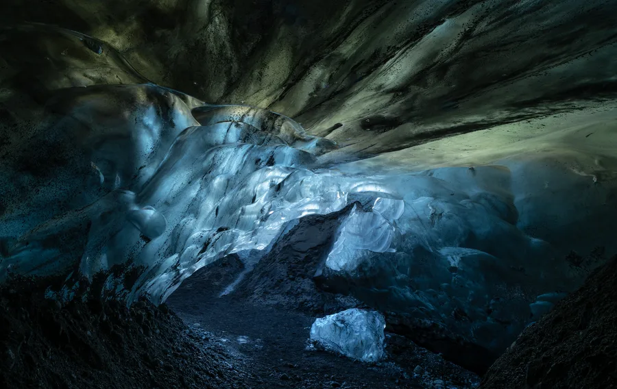 Blue ice cave opening into a dark glacier interior.