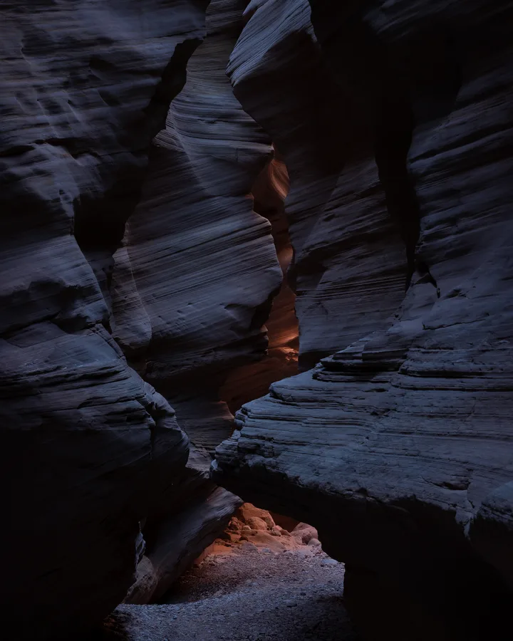 Dark narrow slot canyon with a small warm glow in the passage.