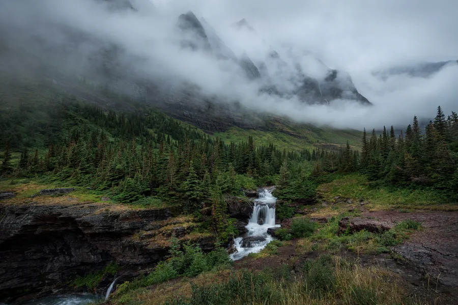 A waterfall flows over rocks in a mountain landscape.