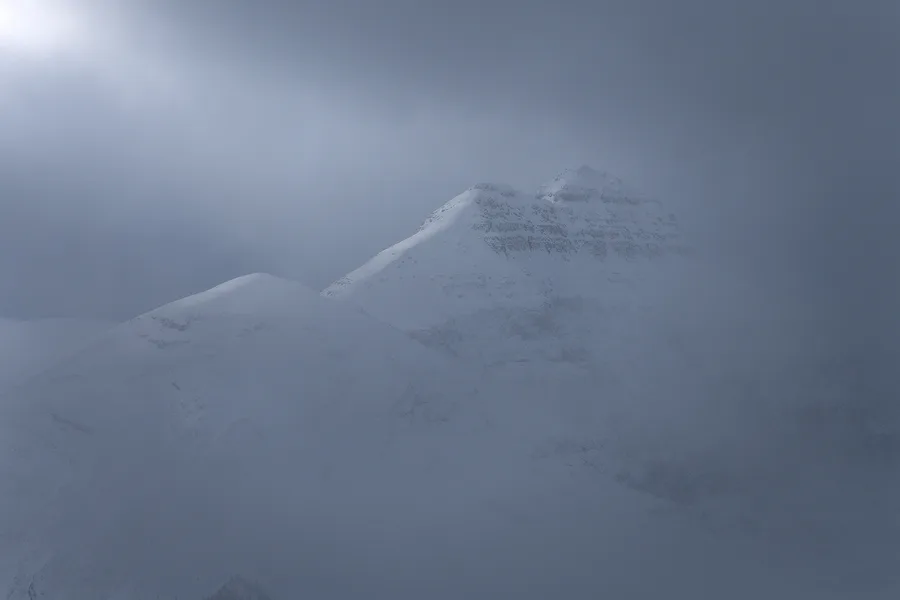 Snowy mountain peak partly hidden in gray mist.