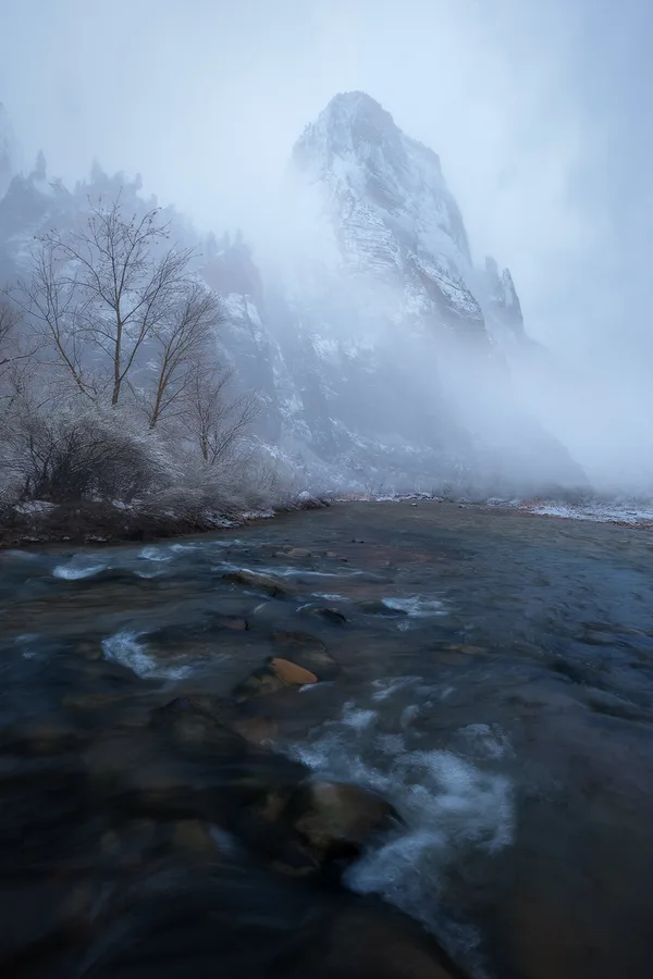 Foggy winter river below a red rock canyon wall.