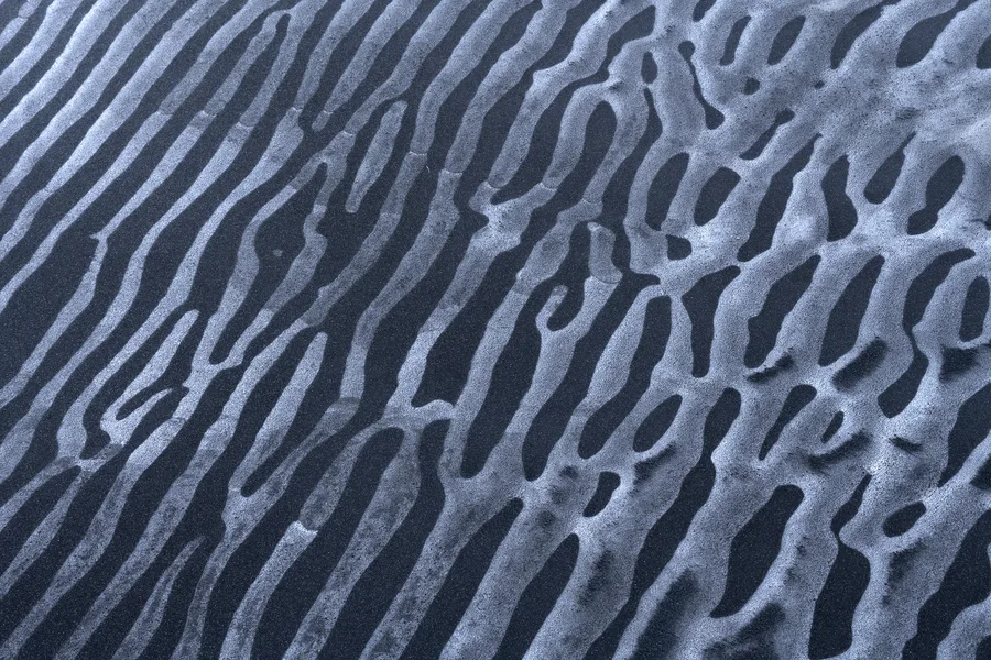 Parallel ripples in black sand and pale ice.