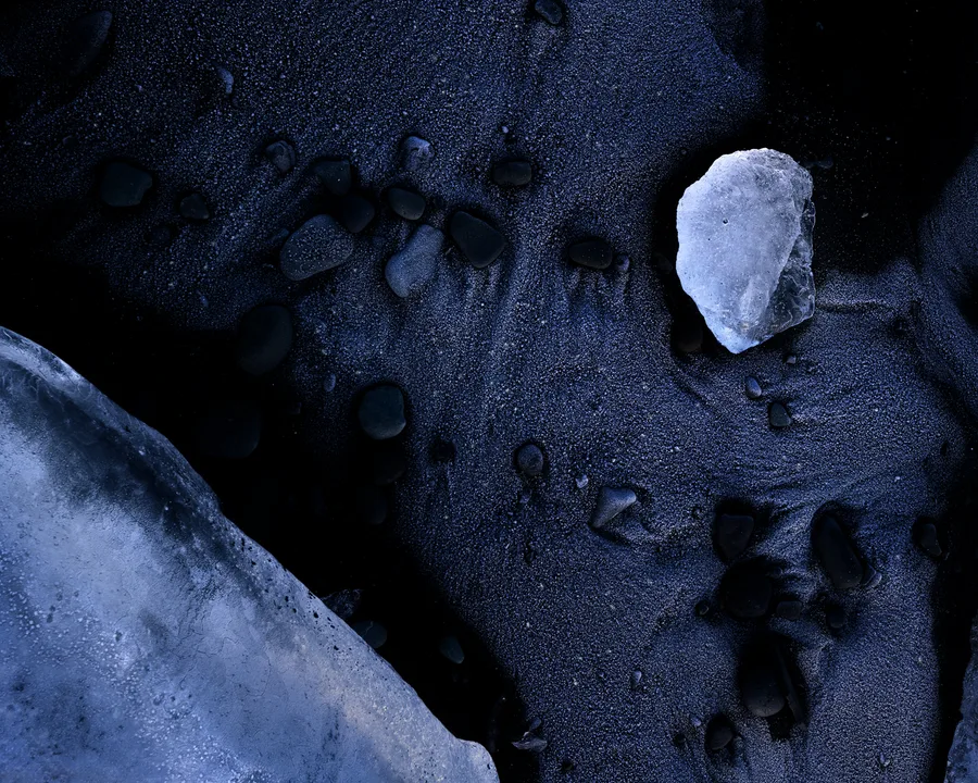 Small white ice fragment on black sand beside blue glacier ice.