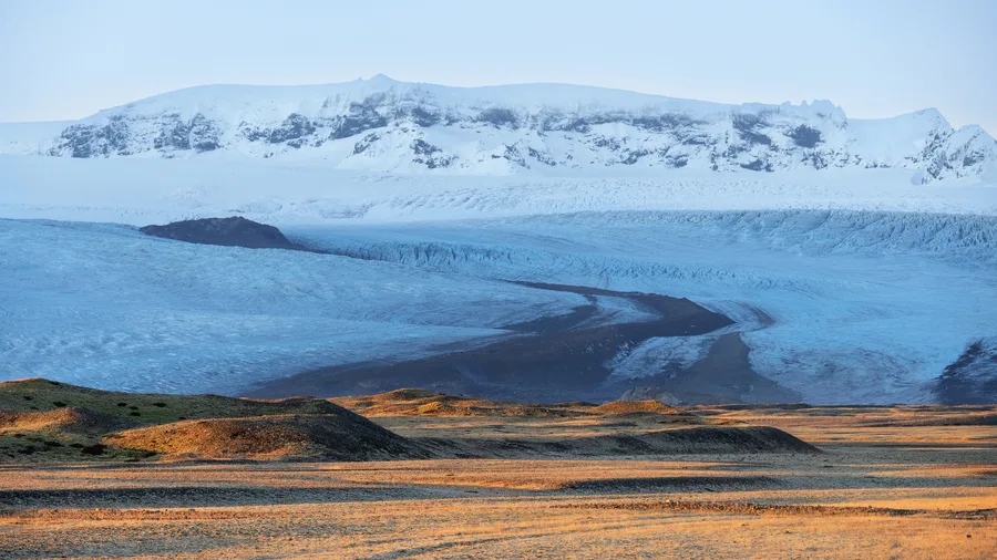 Golden light across black sand and a distant Iceland glacier.