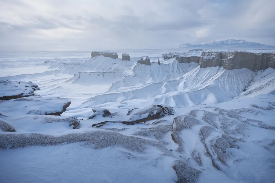 Snow-dusted sandstone cliffs in a canyon beneath a cloudy sky.