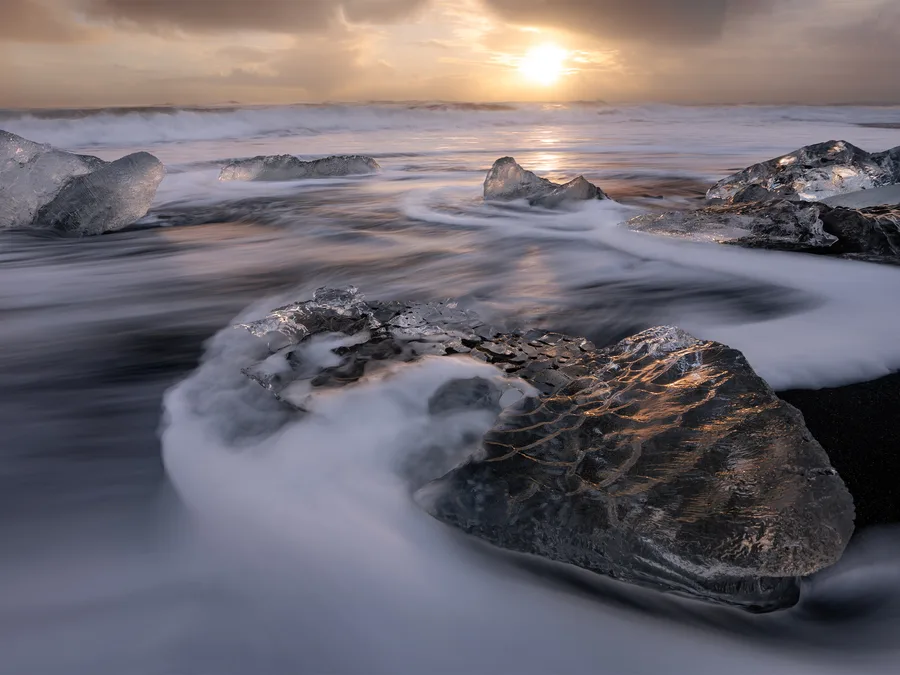 Smooth ocean water moving around ice at golden sunset.