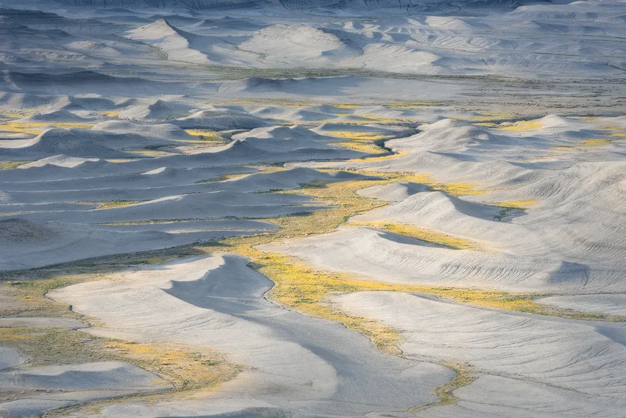 Pale badlands ridges with yellow highlights and gray shadows.