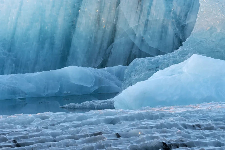 Blue glacier ice and textured frozen layers beside water.