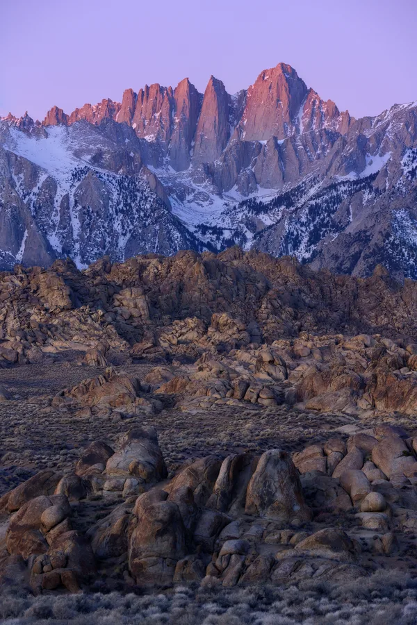 A jagged mountain peak rises above granite ridges at dusk.