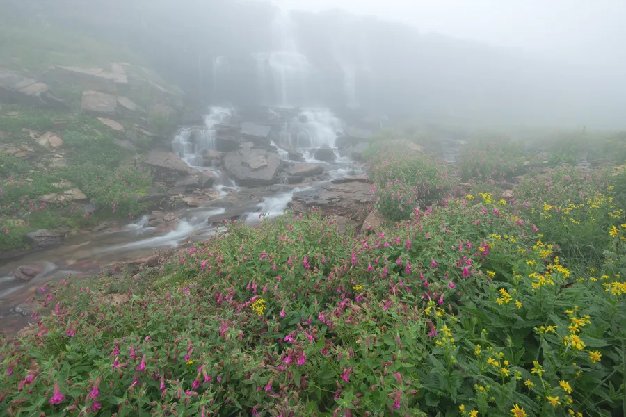 A waterfall flows over rocks in a mountain landscape.