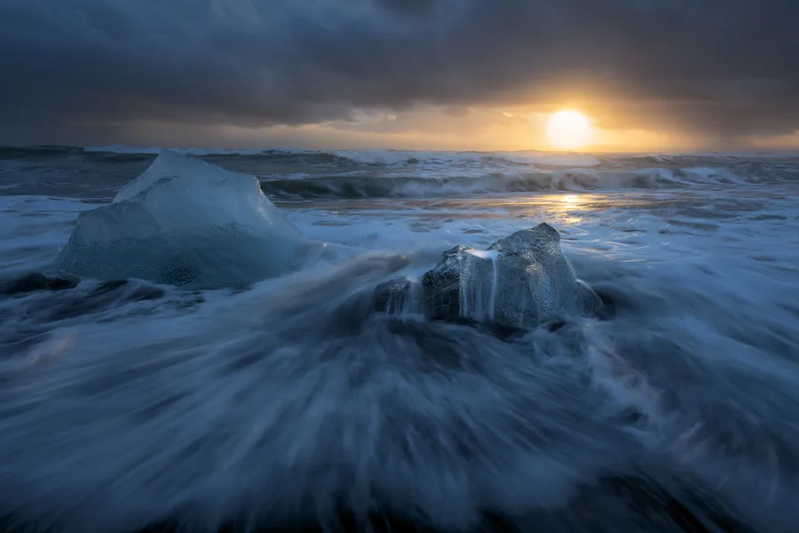 Iceland ocean waves surrounding ice beneath a golden sunset.