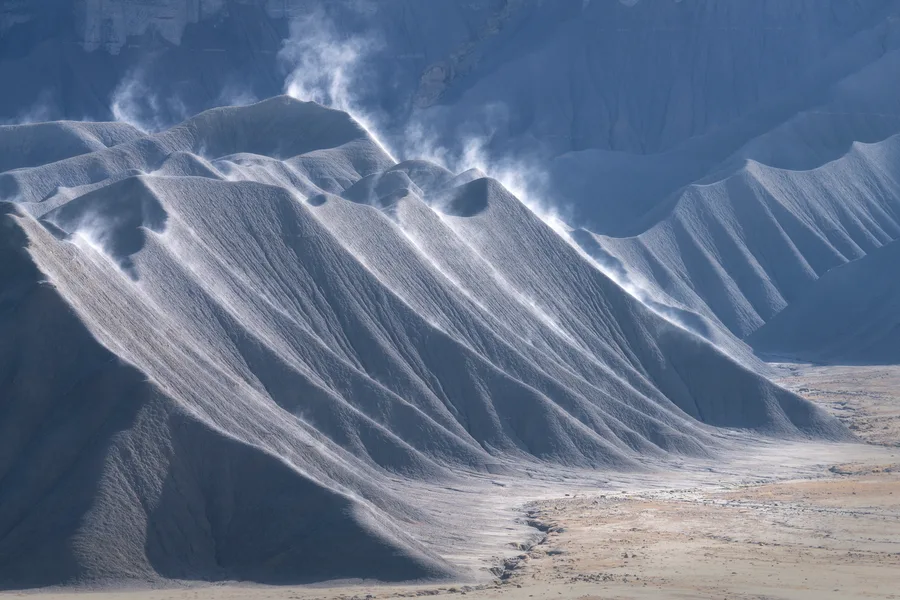 Blue and white eroded badlands ridges with strong shadows.