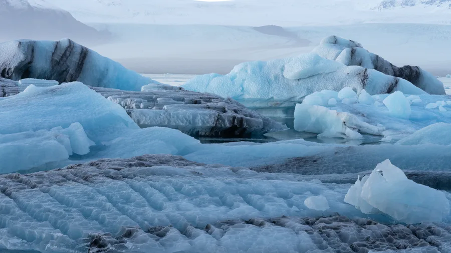 Blue glacier lagoon with scattered icebergs and calm water.