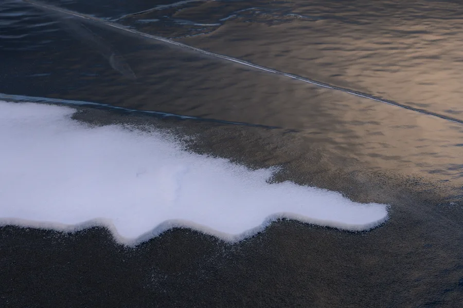 Abstract black shoreline and white snow along a frozen edge.